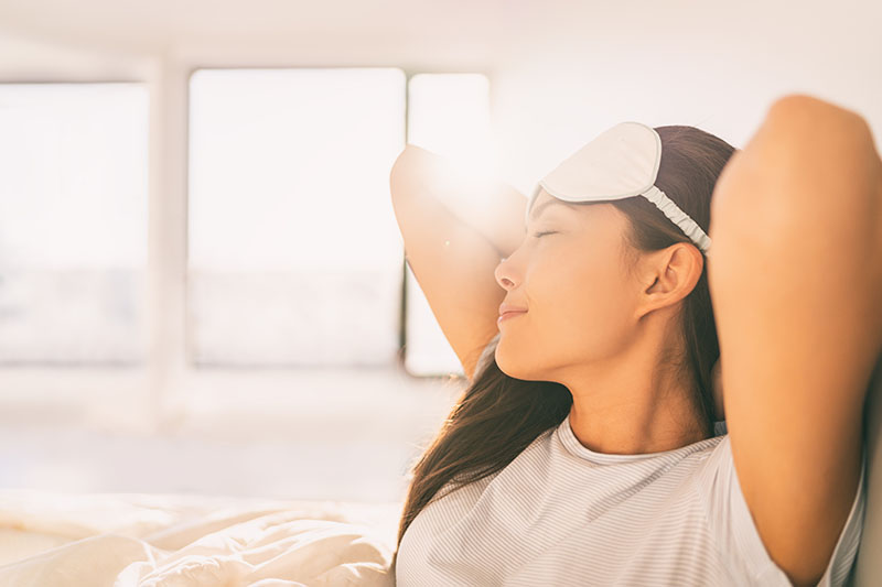 Woman sitting up in bed feeling rested after breathing clean air.