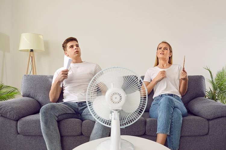 Two people in front of a fan trying to cool down.