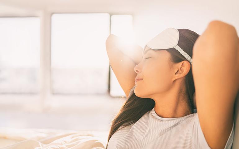 Woman sitting up in bed feeling rested after breathing clean air.