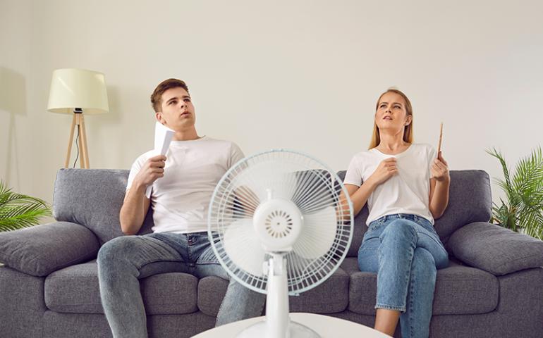 Two people in front of a fan trying to cool down.