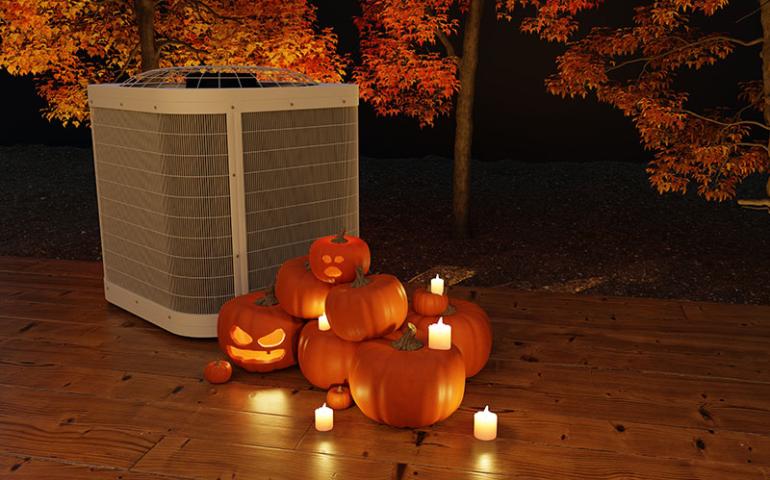 Air conditioning unit with carved pumpkins and candles beside it.