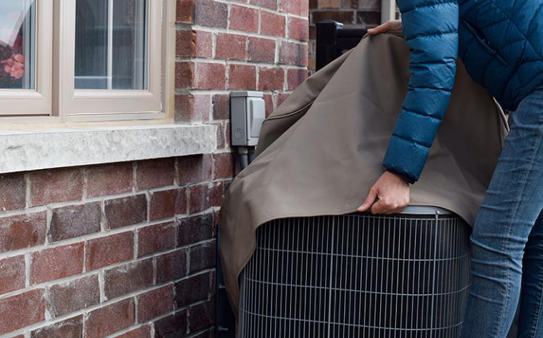 Person putting cover over outside air conditioning unit.